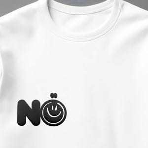 Może przedstawiać: Biała koszulka z okrągłym dekoltem i czarną grafiką. Grafika przedstawia słowo "N&ouml;" z emotikonem uśmiechniętej buzi zastępującym "o". Projekt jest wyśrodkowany na klatce piersiowej.