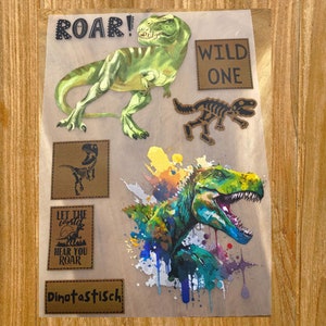 Könnte beinhalten: Ein Set Bügelbilder mit Dinosaurier-Motiven. Die Bügelbilder sind braun, grün und schwarz mit einem Aquarell-Effekt. Die Bügelbilder beinhalten ein Dinosaurierskelett, einen brüllenden Dinosaurier und einen Dinosaurier mit dem Text "Lass die Welt dich brüllen hören!" und "Dinotastic!"