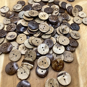 Könnte beinhalten: Ein großer Haufen brauner und natürlicher Kokosnussschalenknöpfe mit verschiedenen Designs, darunter Herzen, Flügel und abstrakte Muster.