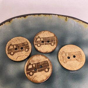 May include: Four wooden buttons with a fire truck design. The buttons are brown with a light brown wood grain pattern. The fire trucks are black and are outlined in a darker shade of brown.