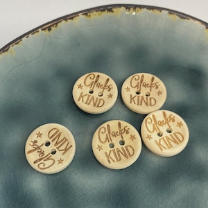 Op de afbeelding: Vijf houten knopen met de woorden "Glücks KIND" en steraccenten, bruin gegraveerd. De knopen zijn gerangschikt op een teal keramische plaat.