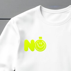 Może przedstawiać: Biała bluza z neonowo-zieloną grafiką z napisem "N&ouml;" i emotikonem uśmiechu. Bluza ma okrągły dekolt i długie rękawy. Grafika jest wyśrodkowana na klatce piersiowej.
