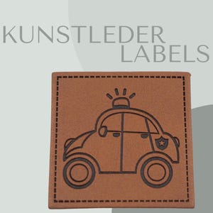 May include: Brown leather patch with a black outline of a cartoon police car with a star on the side. The text "KUNSTLEDER LABELS" is above the patch.