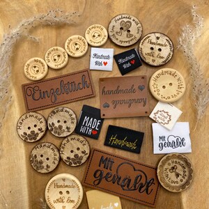 Könnte beinhalten: Sortiment aus Holz-Knöpfen und Stoff-Etiketten mit verschiedenen Designs und Texten, darunter "Handmade with love", "Einzelstick", "handmade" und "Mit genaht".