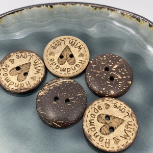 May include: Five round, brown coconut shell buttons with two holes each. Two buttons have the text "Handmade with Love" and a heart design. Three buttons are plain.