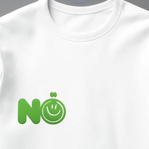 Może przedstawiać: Biała bluza z okrągłym dekoltem z zieloną grafiką. Grafika przedstawia słowo "N&ouml;" ze emotikonem uśmiechu. Projekt jest wyśrodkowany na przodzie koszulki. Bluza wykonana jest z miękkiego materiału.