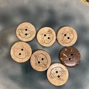 Könnte beinhalten: Sechs Holz-Knöpfe mit Affengesichts-Design und zwei Kokosnuss-Knöpfe mit braunen Flecken.