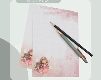 Può includere: Un blocco note DIN A5 da 25 fogli con motivo a griglia e un effetto acquerello rosa. Ogni foglio presenta l'illustrazione di una fata con capelli castani e un vestito rosa. Una matita nera e una penna a sfera verde salvia poggiano sul blocco.
