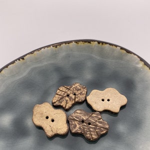 May include: Four brown and beige coconut shell buttons with two holes each, arranged on a blue and brown ceramic plate.