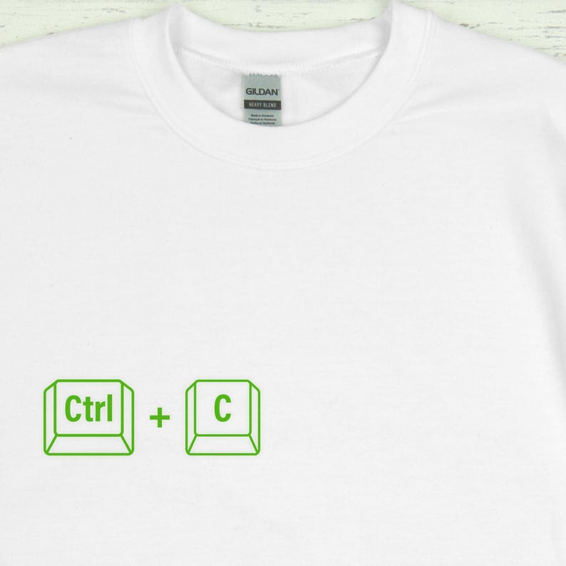 Może przedstawiać: Biała koszulka z okrągłym dekoltem z zieloną grafiką skr&oacute;tu klawiaturowego Ctrl + C. Tekst i symbole są w prostym, obrysowanym stylu. Koszulka ma metkę z tyłu szyi.