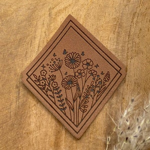 Puede incluir: Un parche de cuero marrón con un diseño floral. El diseño presenta un ramo de flores, hojas y mariposas en un contorno negro.