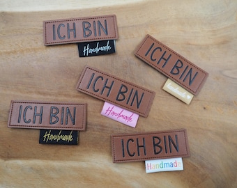May include: Five brown leather labels with the text "ICH BIN" in black lettering. Each label has a smaller black or brown label attached with the word "Handmade" in white or gold lettering.