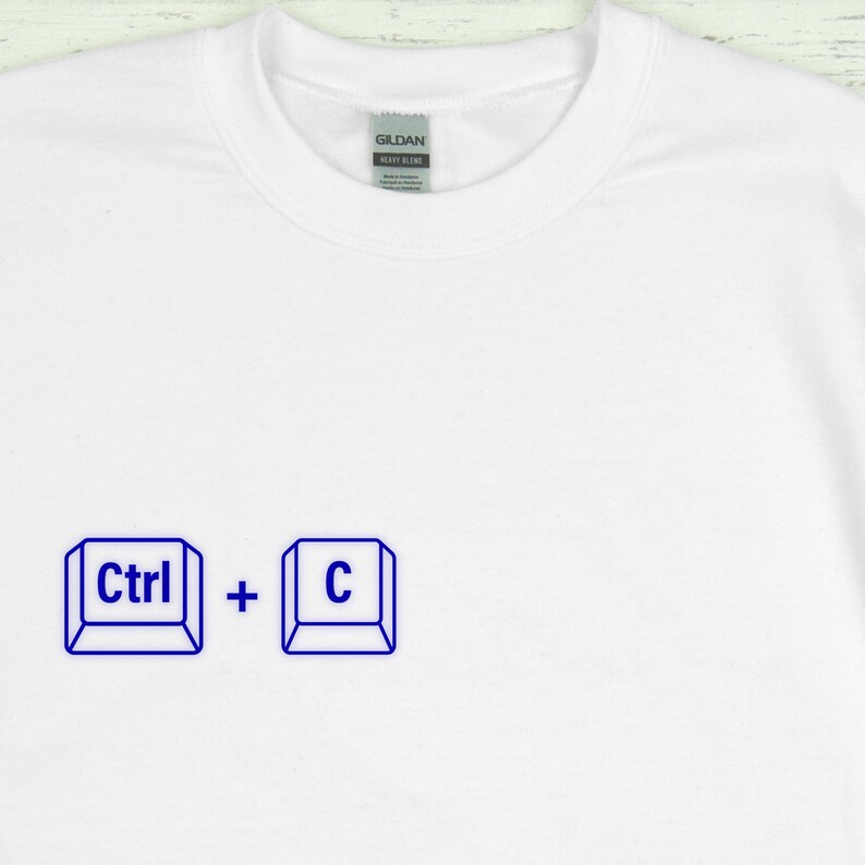 Może przedstawiać: Biała koszulka z niebieską grafiką skr&oacute;tu klawiaturowego "Ctrl + C". Koszulka ma okrągły dekolt i metkę z napisem "Gildan Heavy Blend".