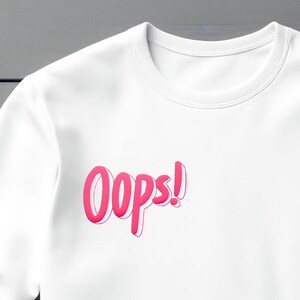 May include: White long-sleeve shirt with a pink "Oops!" graphic printed on the front.