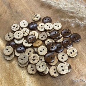 May include: A pile of brown and natural coconut shell buttons with two holes each. The buttons are scattered on a wooden surface.