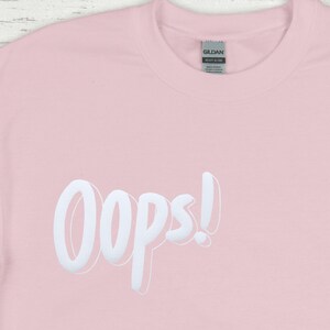 May include: A pink t-shirt with the word "Oops!" printed in white on the front.
