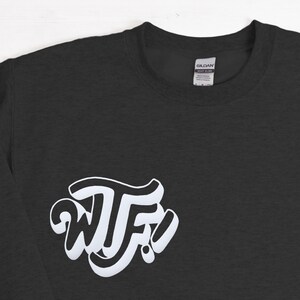 May include: A dark gray long-sleeve t-shirt with a white graphic of the letters "WTF" in a stylized font.