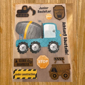 Può includere: Un set di toppe da stirare con veicoli da costruzione e cartelli. Le toppe sono di colore marrone, giallo, blu e nero. Le toppe includono un camion betoniera, un bulldozer, un cartello di stop e un cartello che dice "under construction".