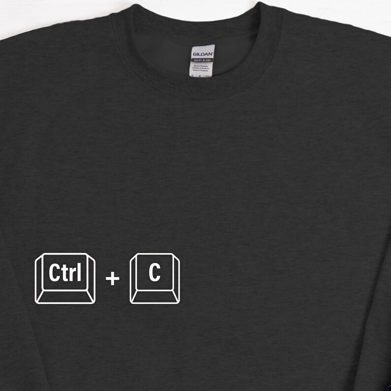 Może przedstawiać: Czarna bluza z białym nadrukiem skr&oacute;tu klawiszowego "Ctrl + C". Bluza marki Gildan ma minimalistyczny design. Idealna dla entuzjast&oacute;w technologii lub fan&oacute;w skr&oacute;t&oacute;w klawiszowych.