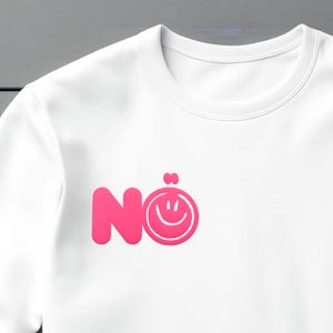 Może przedstawiać: Biała bluza z okrągłym dekoltem z r&oacute;żową grafiką z napisem "N&ouml;" i uśmiechniętą buzią. Bluza wykonana jest z miękkiego materiału i nadaje się do noszenia na co dzień.