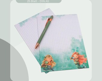 Può includere: Un blocco note con un'illustrazione di sirena e una penna verde con dettagli oro rosa. Il blocco note ha un motivo a griglia e il testo "Notizblock 25 Blatt - DIN A5". L'illustrazione della sirena è nei toni del verde, arancione e giallo.