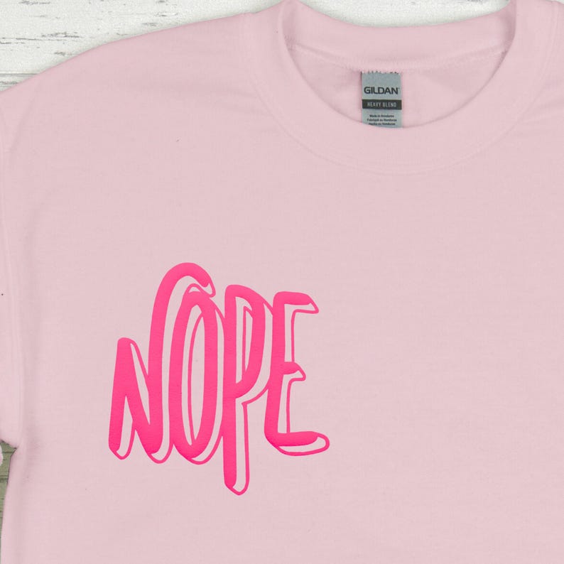 Op de afbeelding: Roze T-shirt met het woord "NOPE" gedrukt in een vet, roze, 3D-lettertype.