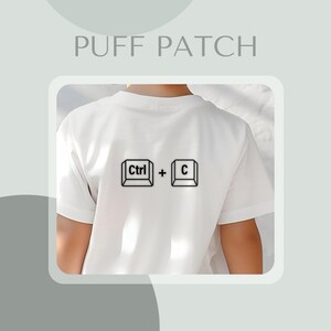 Könnte beinhalten: Weißes T-Shirt mit einer schwarzen Grafik des Tastenkombination Ctrl + C auf dem Rücken. Der Text "PUFF PATCH" befindet sich oben im Bild.