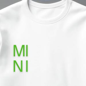 Puede incluir: Sudadera blanca de cuello redondo con la palabra "MINI" impresa verticalmente en letras de bloque verde brillante. La sudadera tiene un estilo cl&aacute;sico e informal.