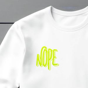 Op de afbeelding: Witte longsleeve met een neon groene grafische afbeelding met de tekst "NOPE" in een vet, gestileerd lettertype.