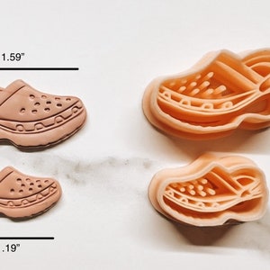 May include: Two light brown clog-shaped objects, one measuring 4.04 cm long and 2.54 cm high, and a smaller one at 3.02 cm long and 1.91 cm high. Two additional objects show the interior of the clog. The objects have a detailed design.