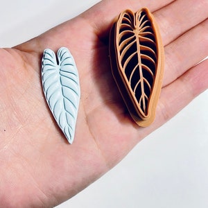Puede incluir: Un par de moldes de silicona en forma de hoja. Un molde es azul claro y el otro es marr&oacute;n. Los moldes est&aacute;n dise&ntilde;ados para crear decoraciones en forma de hoja.