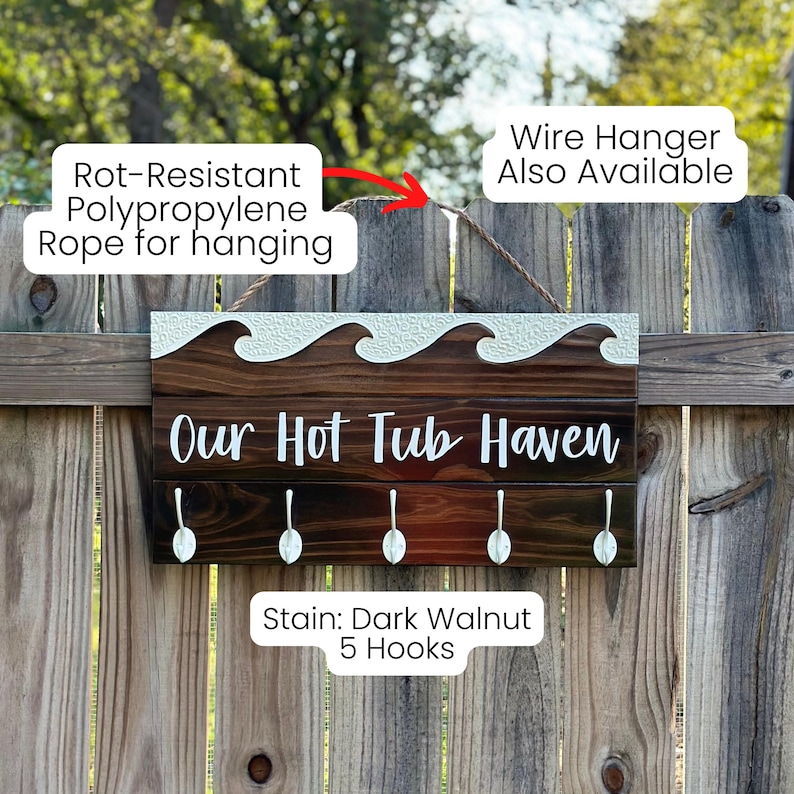 K&ouml;nnte beinhalten: Dunkel walnussfarbenes Holzschild mit dem Text "Our Hot Tub Haven" und f&uuml;nf Haken. Das Schild hat ein Wellendesign und ein Polypropylen-Seil zum Aufh&auml;ngen. Ein dekorativer Artikel.