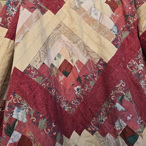 May include: A patchwork quilt with a geometric design. The quilt is made from red and cream-coloured fabric strips. The red fabric has floral patterns, and the cream-coloured fabric has a subtle pattern. The quilt is handmade.