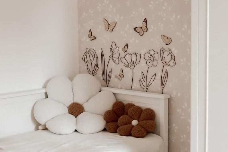 May include: A bedroom scene featuring a white bed with a large, daisy-shaped pillow and a smaller, brown flower pillow. The wall is decorated with wooden butterfly and flower cutouts, creating a whimsical, nature-inspired theme.
