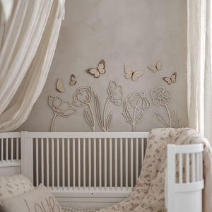 May include: A nursery scene featuring a white crib with a floral patterned blanket and pillow with the word "love". The wall is decorated with wooden cut-out flowers and butterflies in a neutral color palette.