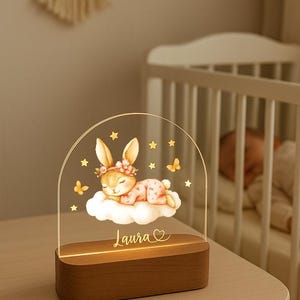 May include: A decorative night light featuring a sleeping bunny on a cloud, with stars and butterflies. The base is wood, and the name "Laura" is inscribed. The light is designed for a nursery or child's room.