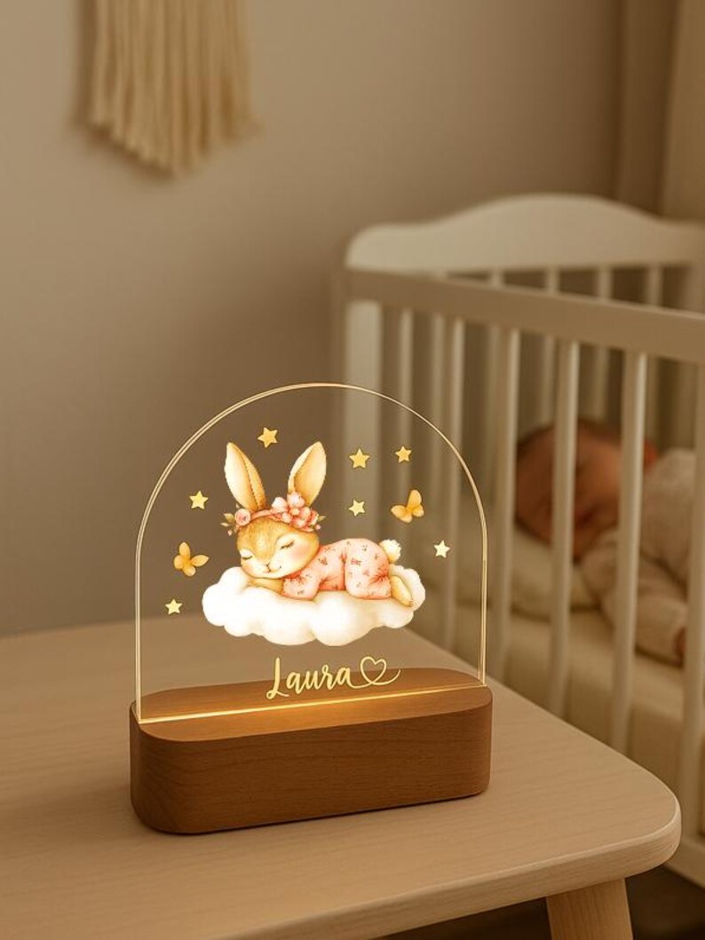 May include: A decorative night light featuring a sleeping bunny on a cloud, with stars and butterflies. The base is wood, and the name "Laura" is inscribed. The light is designed for a nursery or child's room.