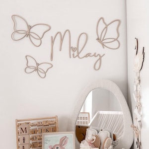 May include: A set of three ceramic mugs with a speckled, cream-colored glaze. Each mug features a different hand-painted design: a blue and green leaf, a yellow flower, and a red berry. The mugs have a simple, rounded shape.