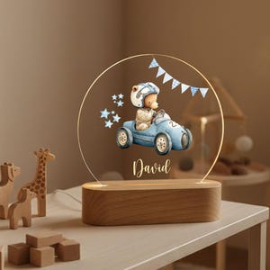 May include: A decorative night light featuring a bear in a race car design. The light has a wooden base and a clear acrylic panel with the name "David" printed on it. The bear is wearing a helmet and the car is blue.