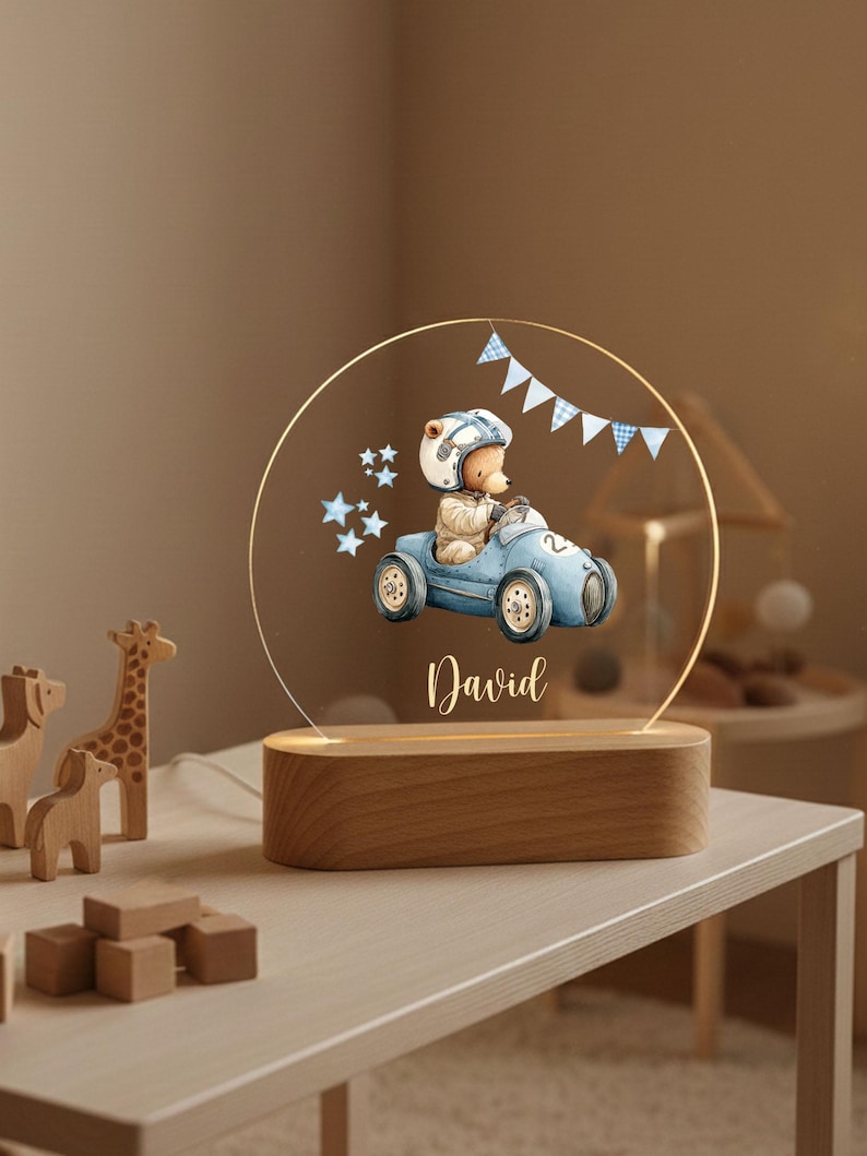 May include: A decorative night light featuring a bear in a race car design. The light has a wooden base and a clear acrylic panel with the name "David" printed on it. The bear is wearing a helmet and the car is blue.
