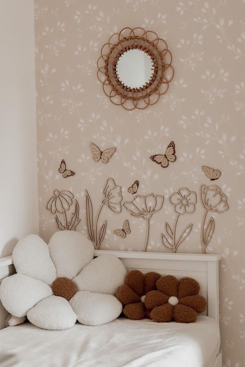 May include: A bedroom scene featuring a floral theme. A round woven mirror hangs above wooden flower and butterfly wall decor. Two flower-shaped pillows, one white and one brown, rest on a white bed.