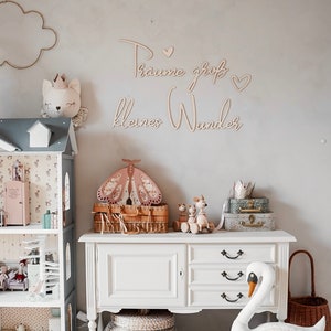 May include: A white dresser with three drawers and a white swan plush toy sitting on a gray cushion. The dresser is decorated with a wooden sign that reads "Traume gro&szlig; kleines Wunder" and a wooden butterfly.