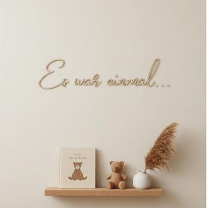 May include: A wooden shelf displays a teddy bear, a book with a bear illustration, and a small white vase with dried pampas grass. Above, the phrase "Es war einmal..." is written in cursive.