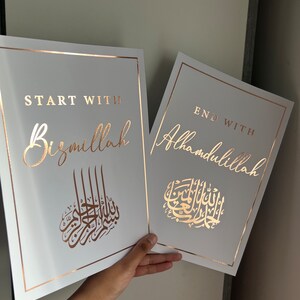 May include: Two white framed prints with gold borders. The print on the left says "Start with Bismillah" in gold lettering with a gold Arabic calligraphy design. The print on the right says "End with Alhamdulillah" in gold lettering with a gold Arabic calligraphy design.