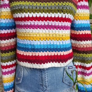 Puede incluir: Un top de crochet a rayas de colores con mangas largas. El top está hecho con un punto texturizado y tiene un ajuste holgado. El top se combina con una falda vaquera azul.