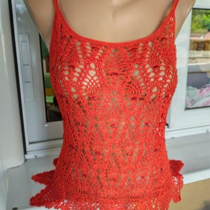 May include: A red crocheted tank top with a scalloped hem. The top is made of a delicate, open-weave fabric.