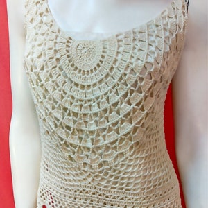 May include: A crocheted tank top with a white, cream color. The top has a scalloped hem and a circular pattern.