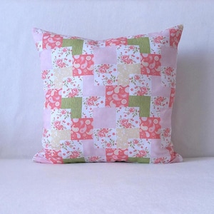 Könnte beinhalten: Quadratisches Zierkissen mit Patchwork-Design. Das Kissen hat Quadrate aus rosa, grünen und cremefarbenen Stoffen mit Blumen- und Paisley-Mustern. Das Kissen ist rosa.