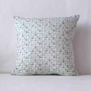 Könnte beinhalten: Quadratisches Kissen mit hellblauem Hintergrund und einem sich wiederholenden Muster aus weißen und roten Blumenformen. Ein weiches, komfortables Wohnaccessoire.