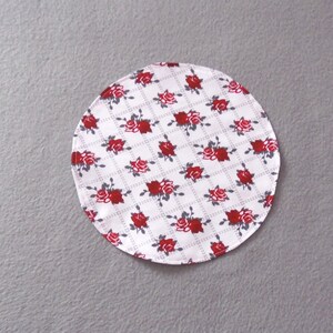 Könnte beinhalten: Runder Stoffuntersetzer in Weiß mit einem roten Rosenmuster auf grauem Hintergrund.